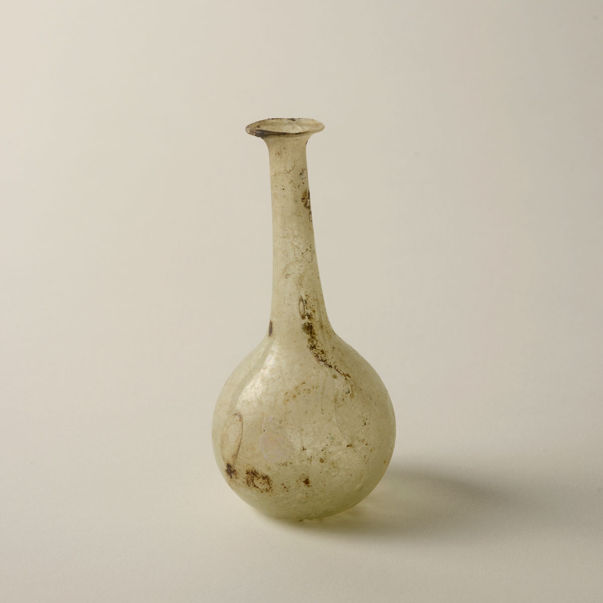 Delicate, opaque white glass bottle with a long, slim neck and spherical base, appearing aged and weathered.