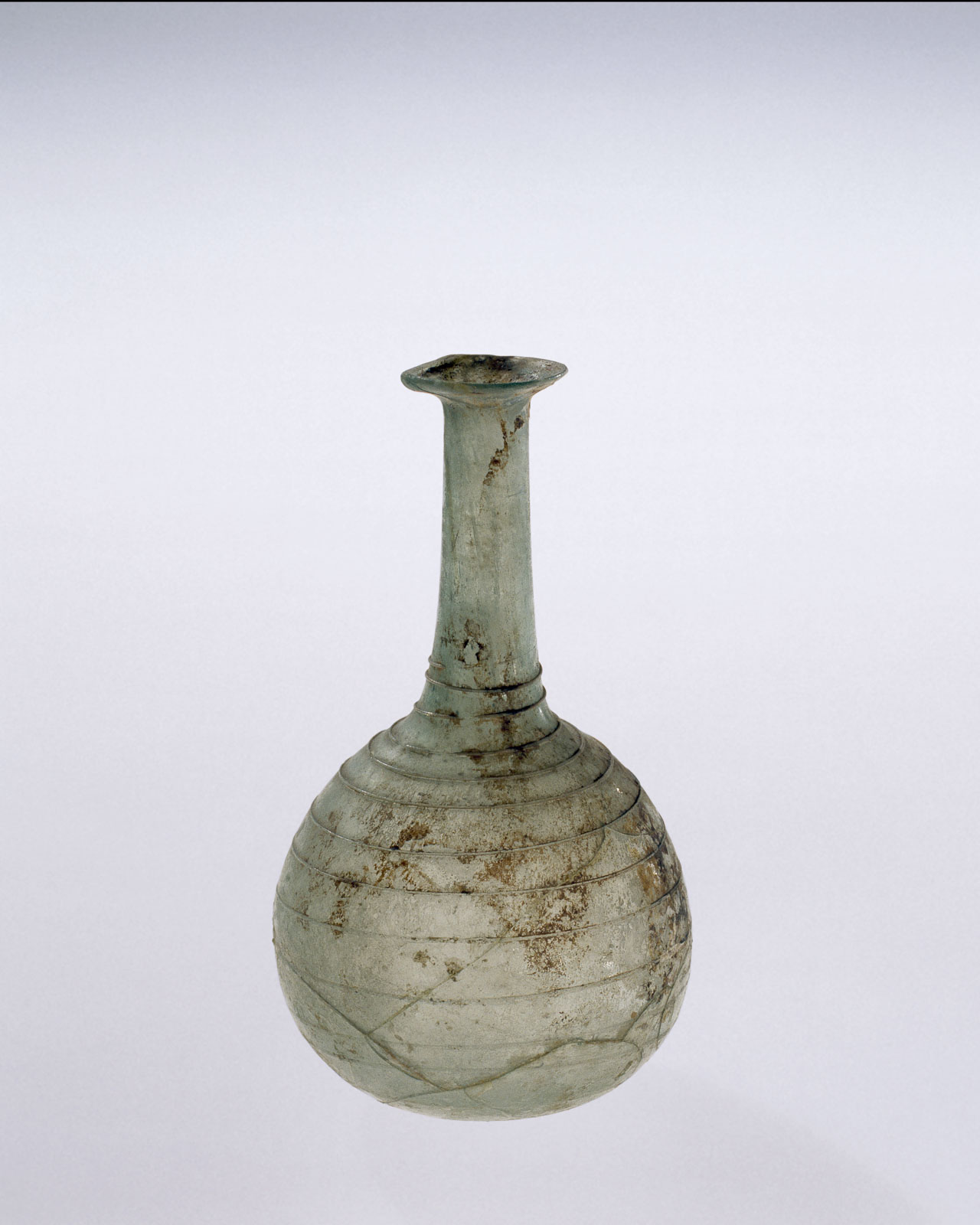 Elongated glass vessel with a slender neck, rounded body, and spiral line decoration, showing signs of age