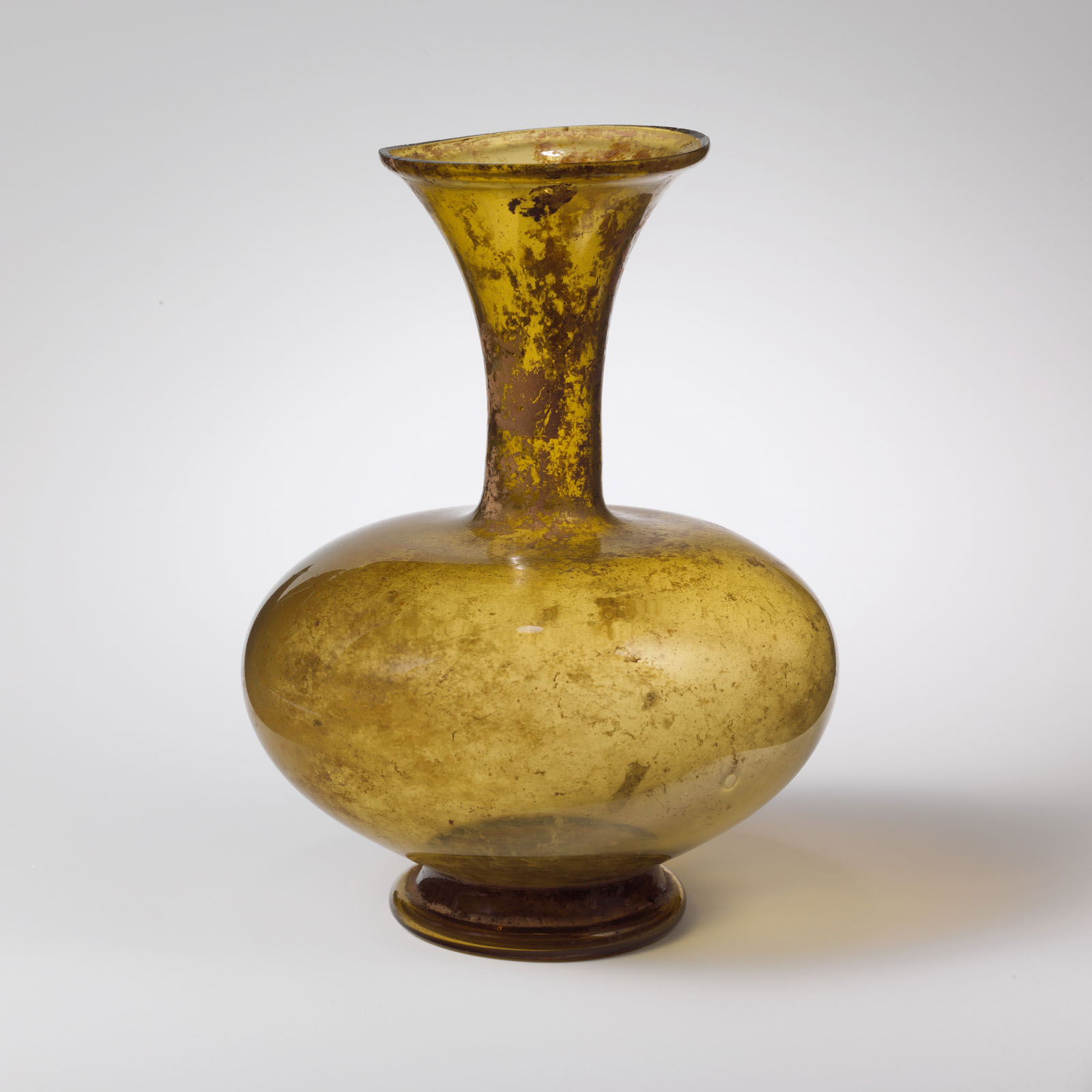 Mottled golden-yellow glass bottle with a flared neck and bulbous base, exhibiting a weathered surface.