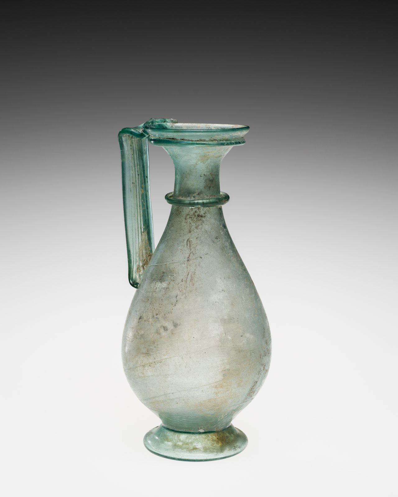 Pale blue glass jug with a handle and a tapered neck above a rounded body and foot