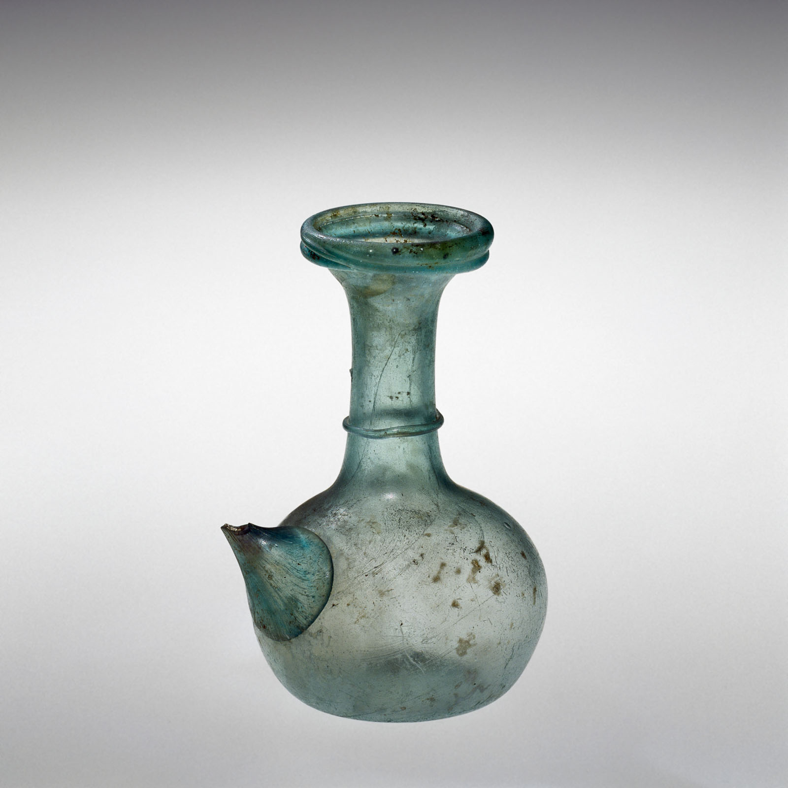 Blue-green glass vessel with a spout, showcasing a bulbous body and a flared neck, showing signs of age