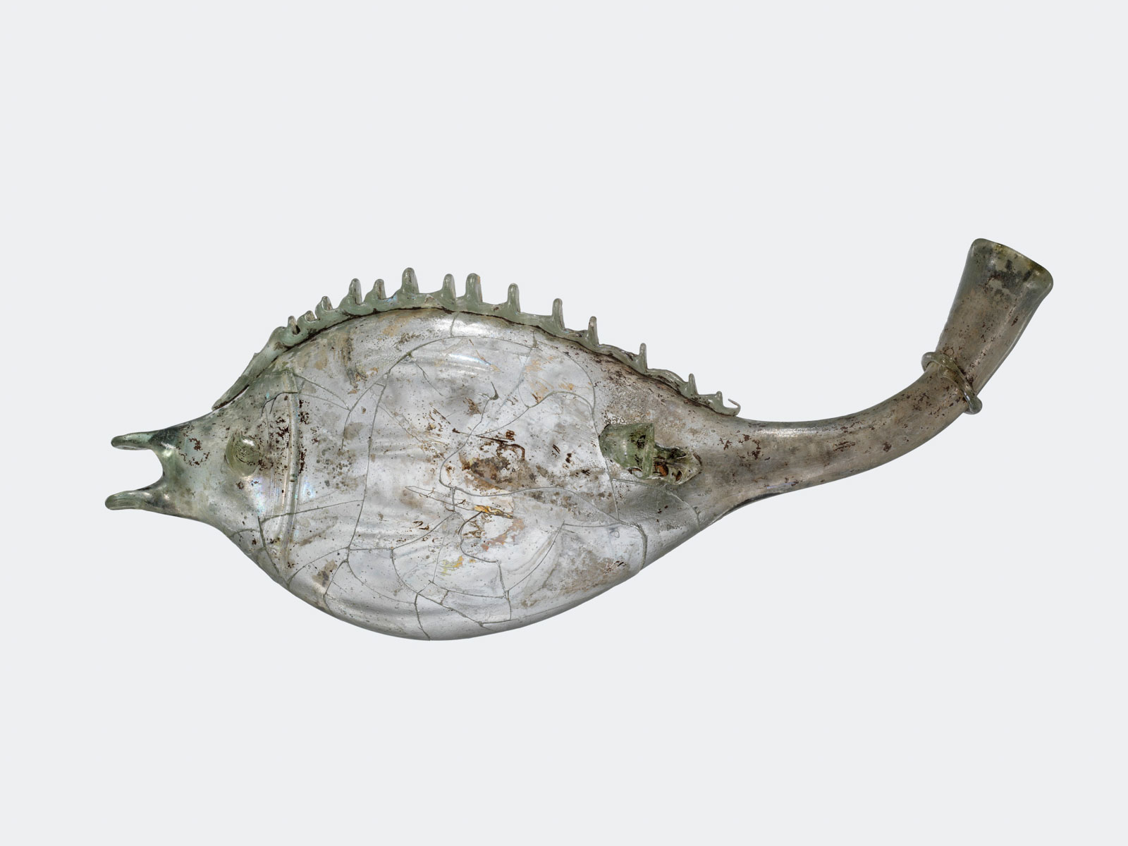 Pale greenish cracked glass vessel with fish silhouette, dorsal fin detail, and round open tail, showing signs of aging