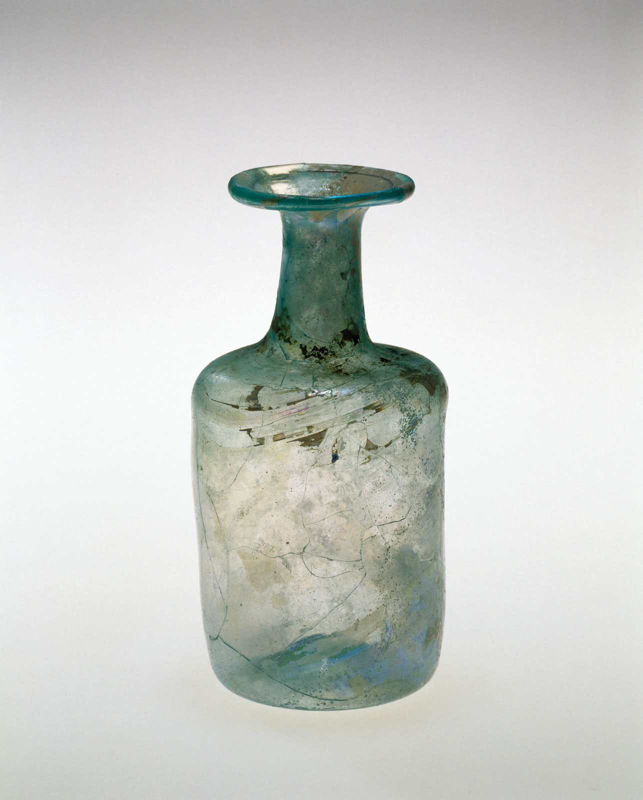 Uneven, cylindrical blue-green glass bottle exhibiting a wide, flat rim and a surface marked by extensive crackling