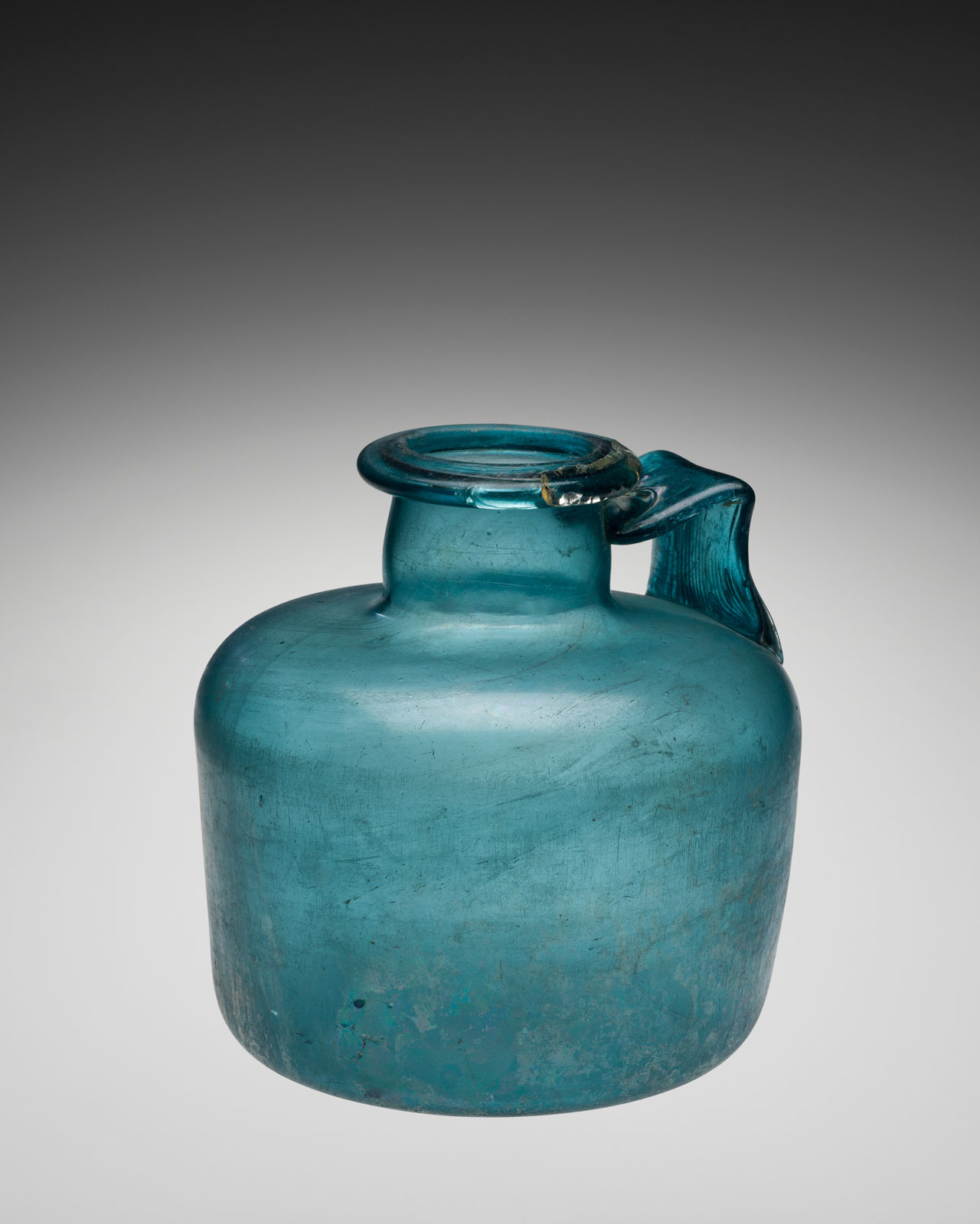 Squat, teal glass jar with a single handle and rolled rim