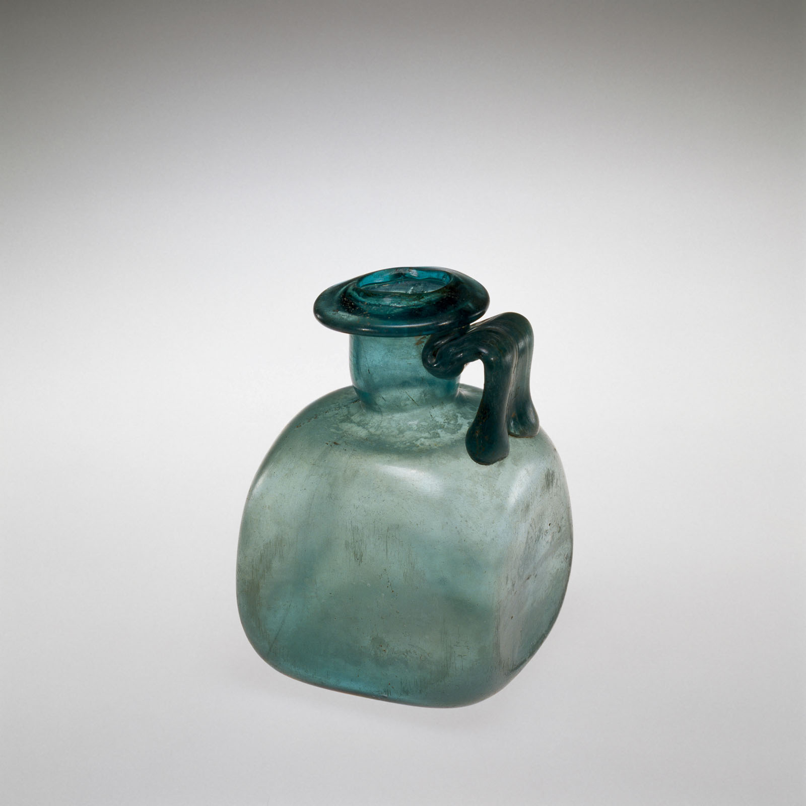 Blue-green glass jug with a squared, stout body and single flat handle