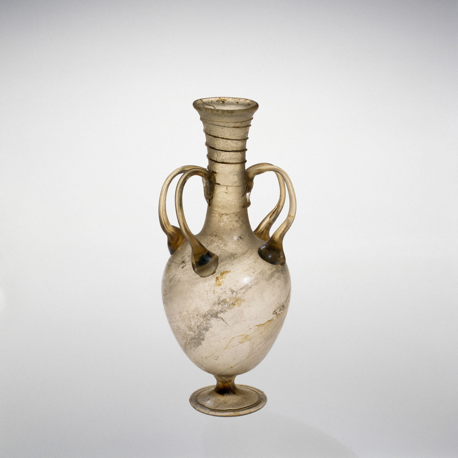 Glass vessel with four round handles, a spiraled neck and bulbous body, standing on a circular foot, showing signs of aging