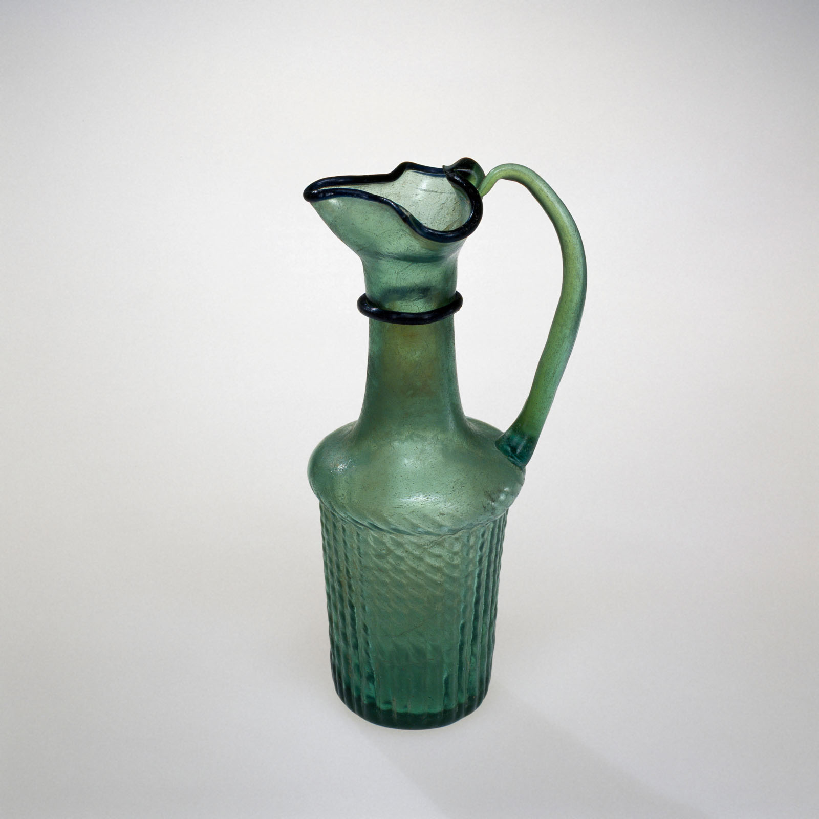 Green glass jug with a flared spout, patterned flat-bottomed body, and a rounded handle