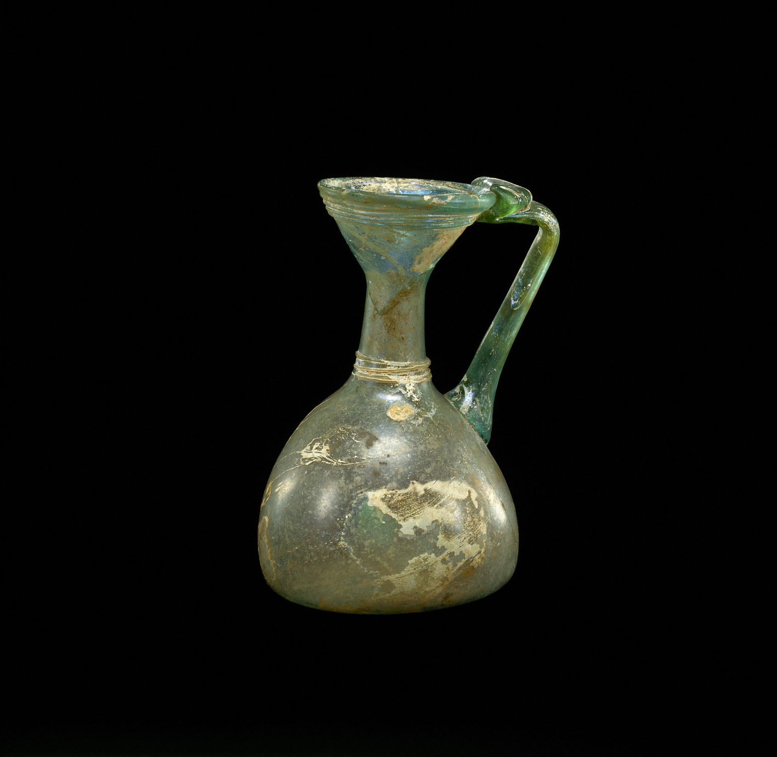 Translucent green glass pitcher with a wide base narrowing to a flared top, paired with a rounded handle, showing signs of aging