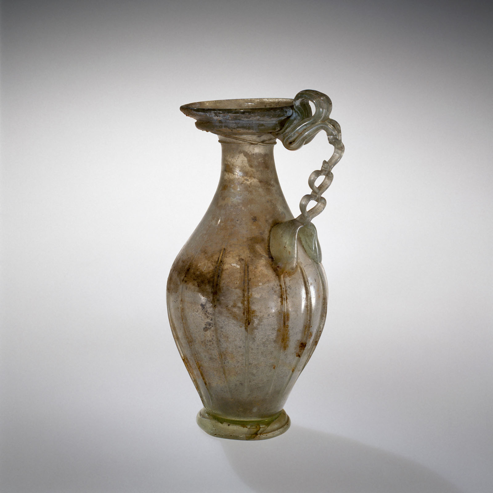 Translucent glass vessel with vertical ribbing and a delicate twisted handle, with a weather iridescent surface