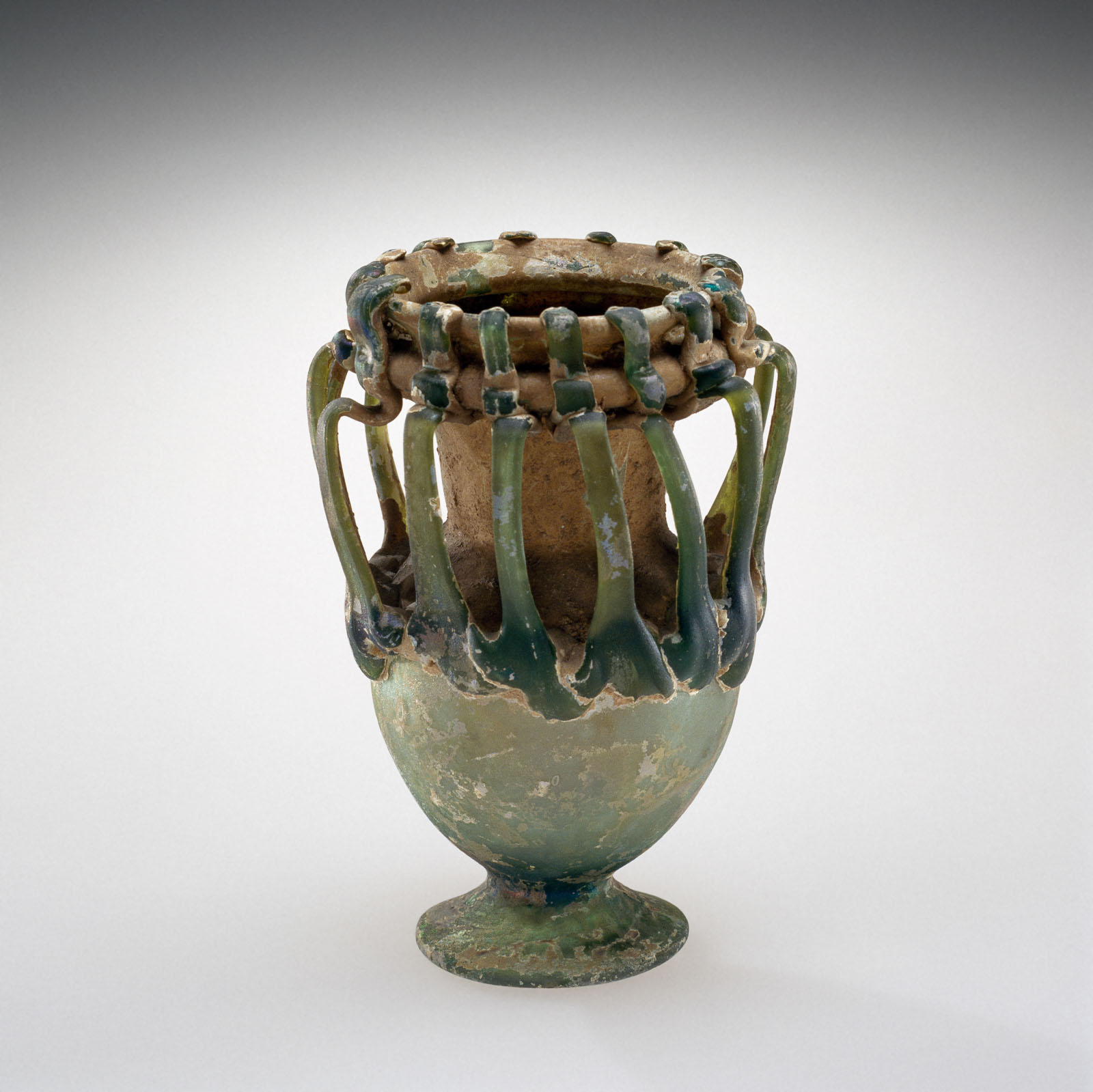 Mottled glass jar with a wide rim and numerous uneven rounded handles, showing extensive signs of aging