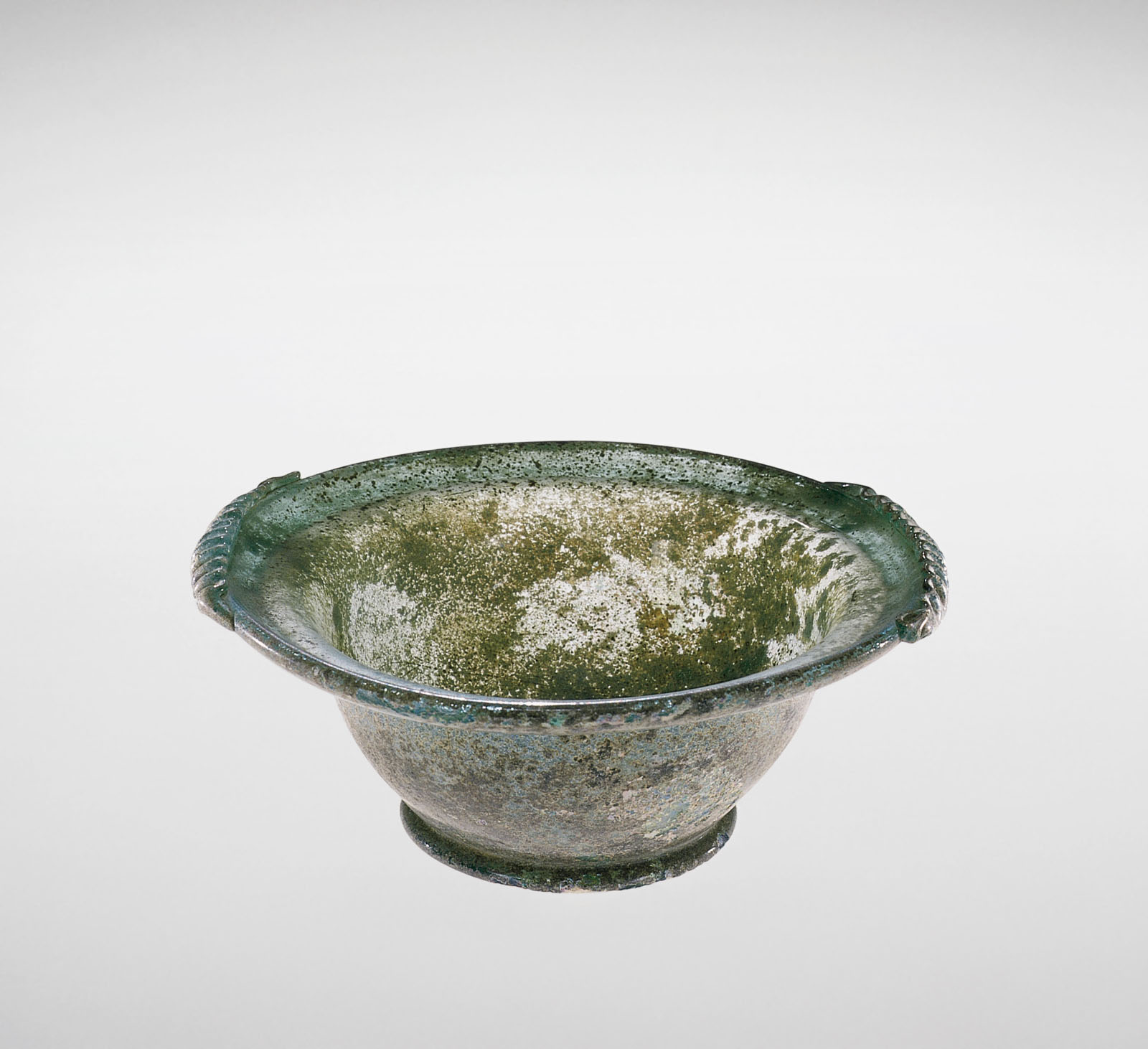 Mottled green glass bowl with a flared, scalloped handles, showing extensive signs of aging