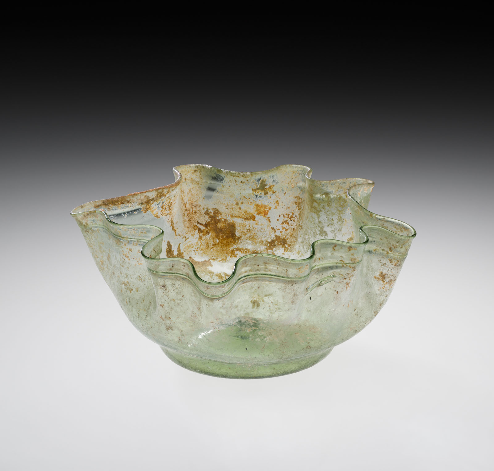 Mottled green glass bowl with a wavy, undulating rim; extensive signs of aging