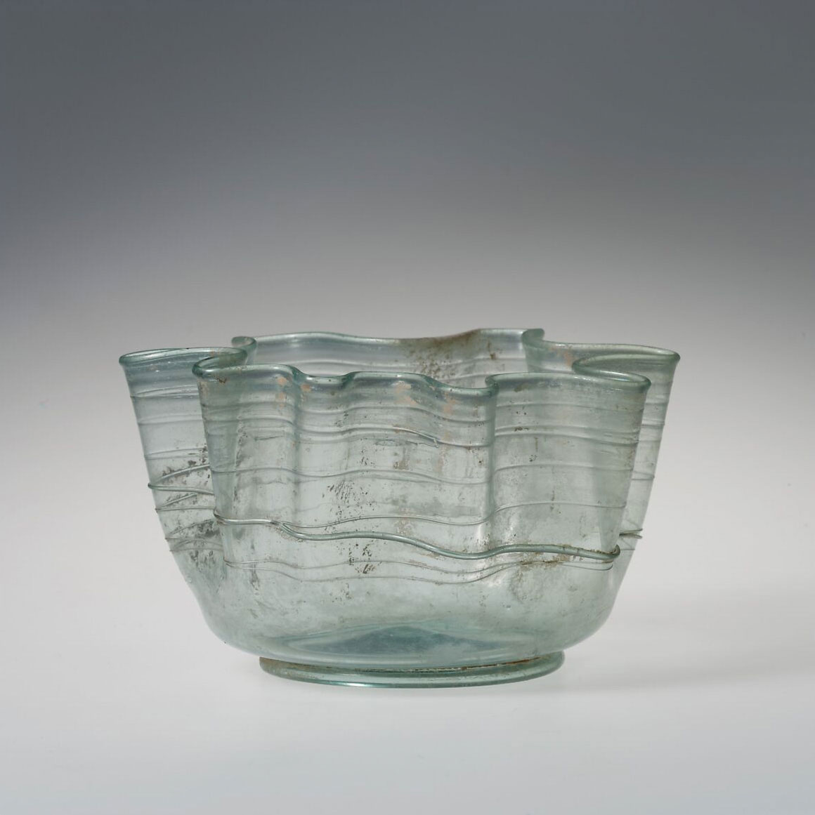 Translucent glass bowl with a ribbed design, undulating rim, and a hint of a blue-green tint