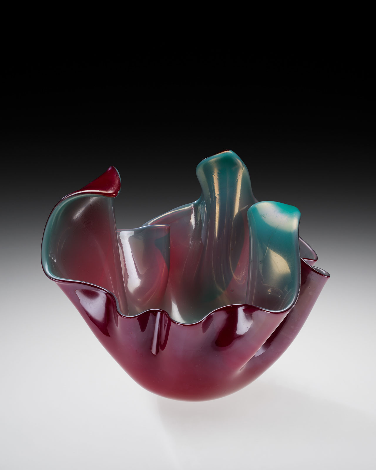 A modern glass bowl with vibrant dark red to teal gradients and wavy, undulating shape