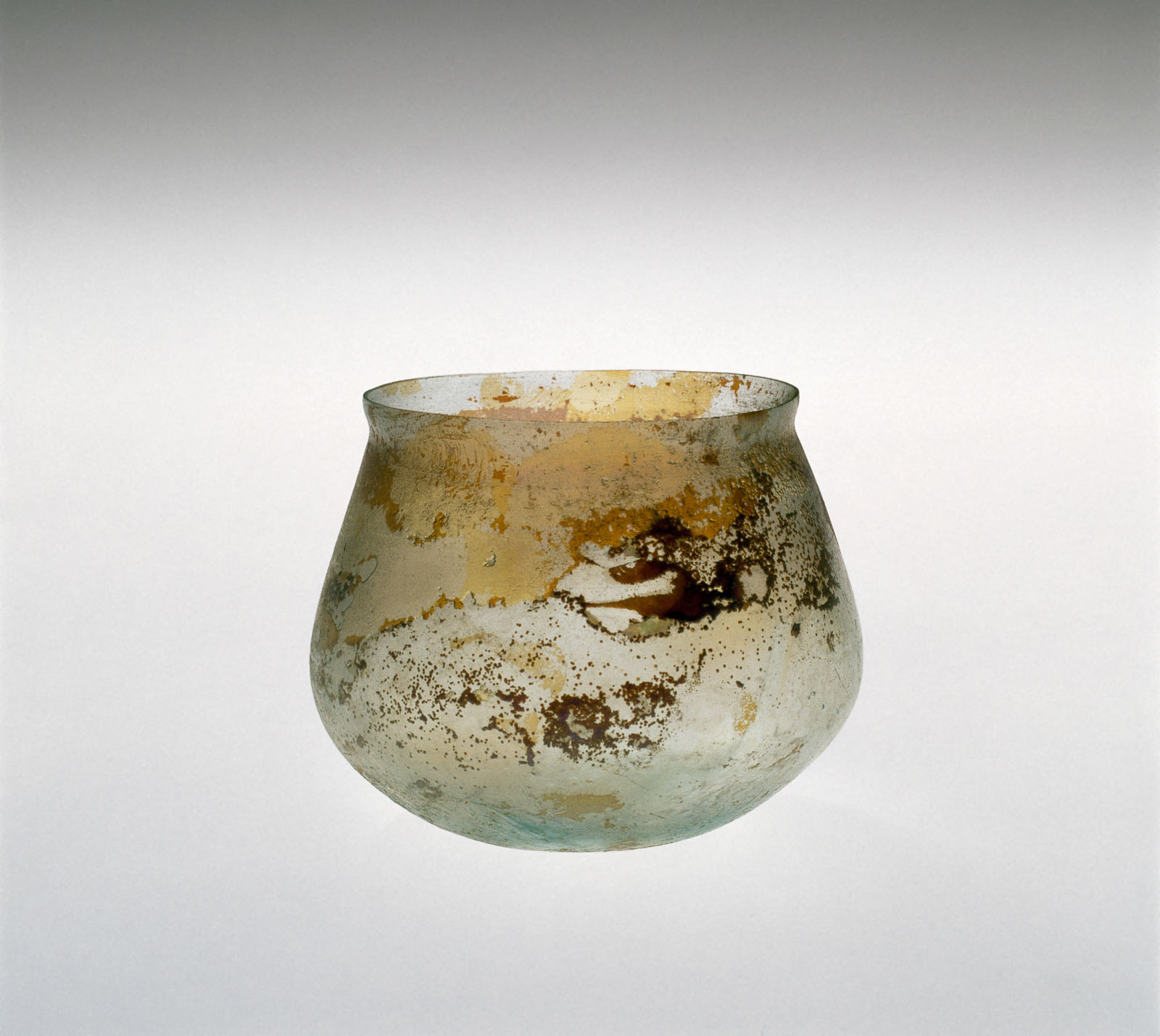 Semi-transparent glass cup with a round bottom and a mottled appearance, showing extensive signs of aging