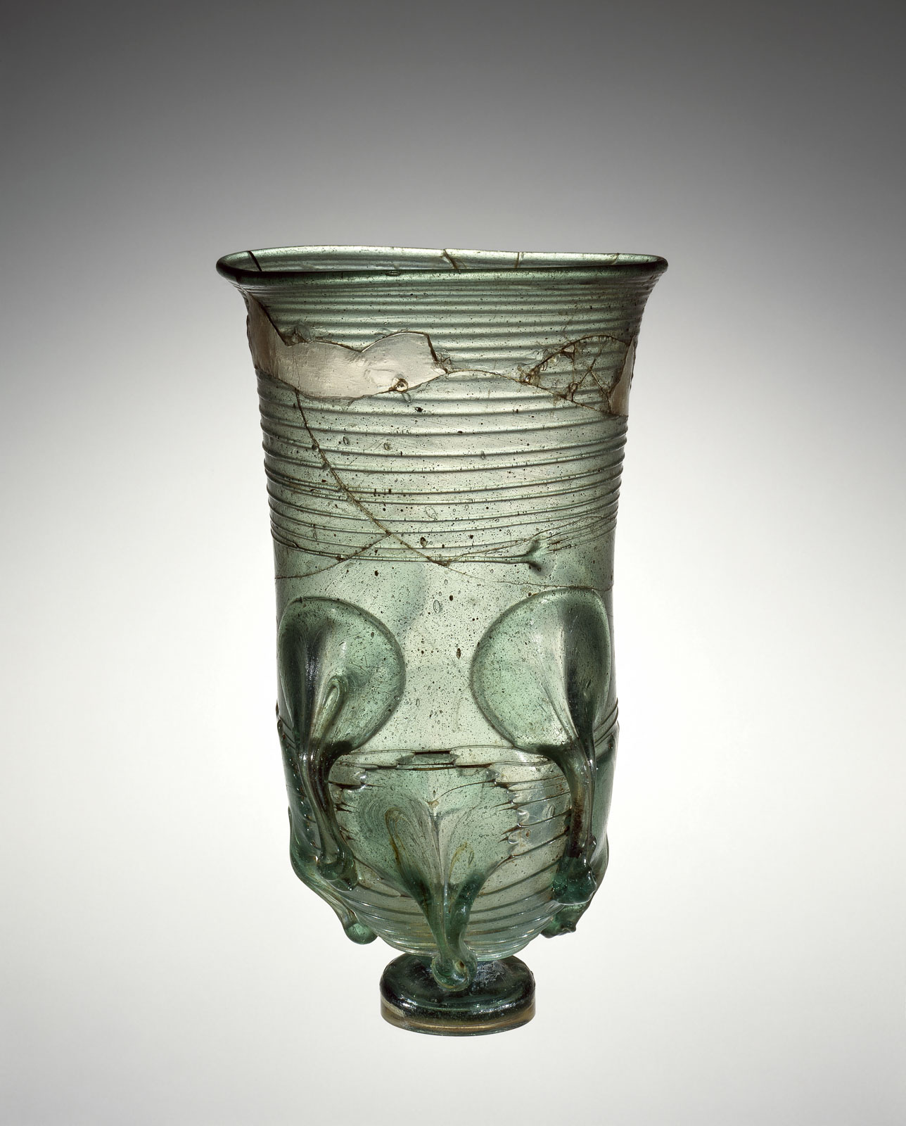 Cracked, greenish glass beaker with embossed circular leaf and banded patterns and small round foot