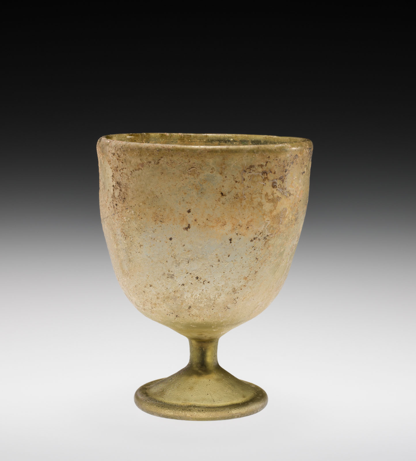 Simple pale yellow- green goblet with short sten, showing extensive signs of aging