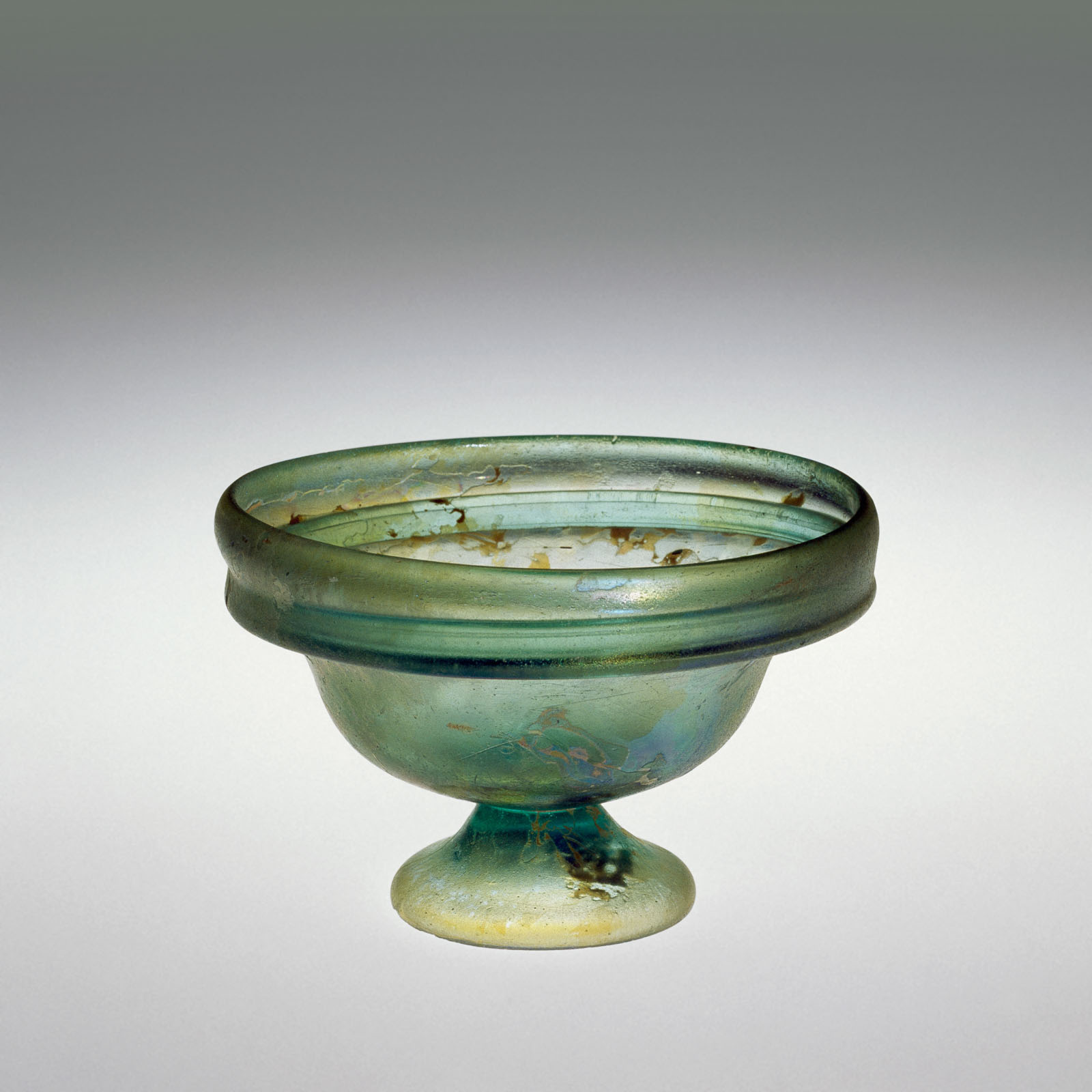 Short, shallow green glass bowl with a flat wide rim, supported by a short flared base, showing signs of aging