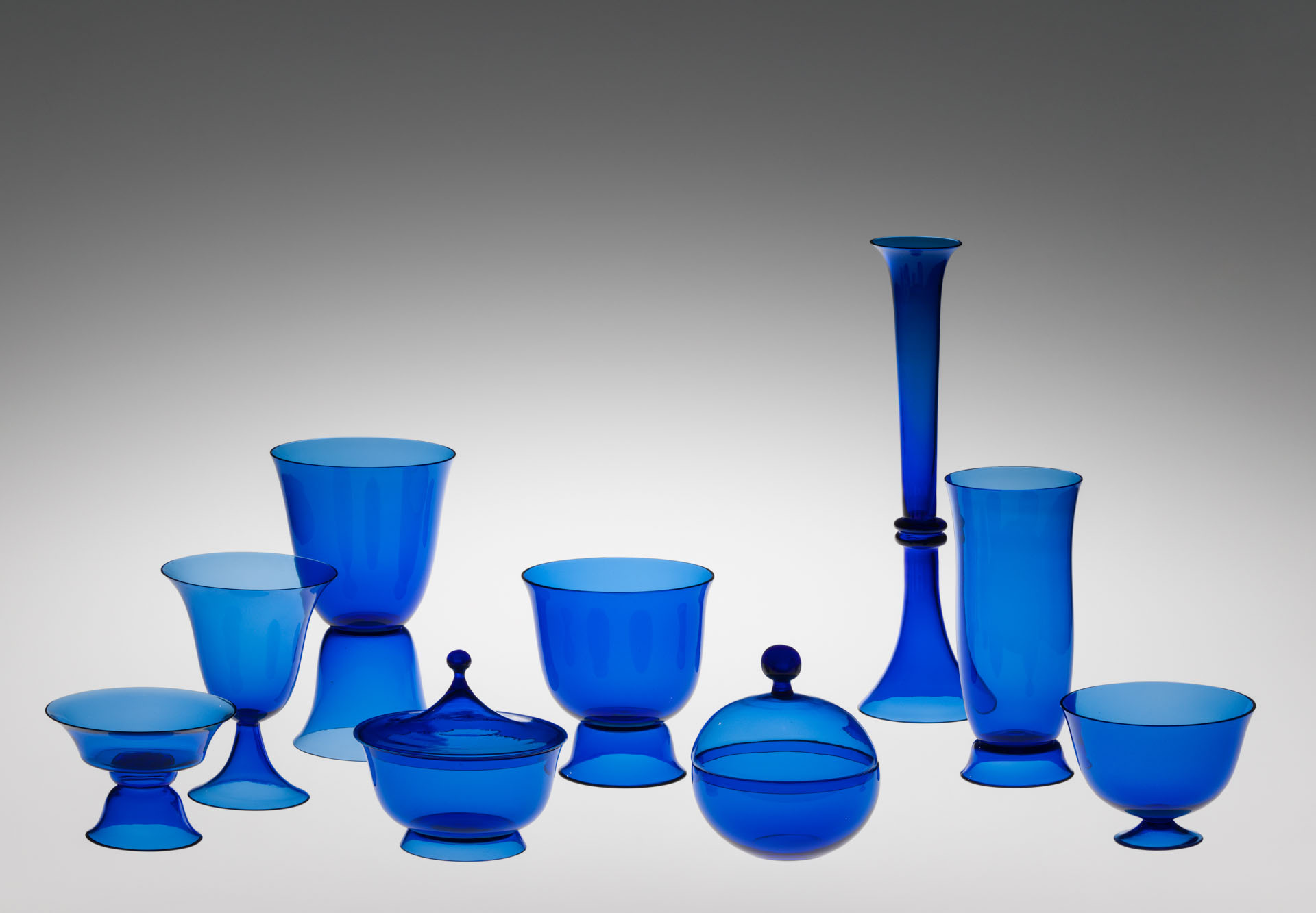 Assortment of modern, vibrant, cobalt blue glass vessels, including various goblets, tall vases, and lidded containers